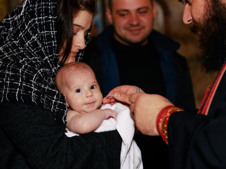 A traditional Orthodox baptism featuring a priest, baby, and family in an intimate ceremonial setting.