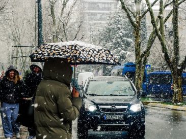A snowy city street with people carrying umbrellas and cars passing by.