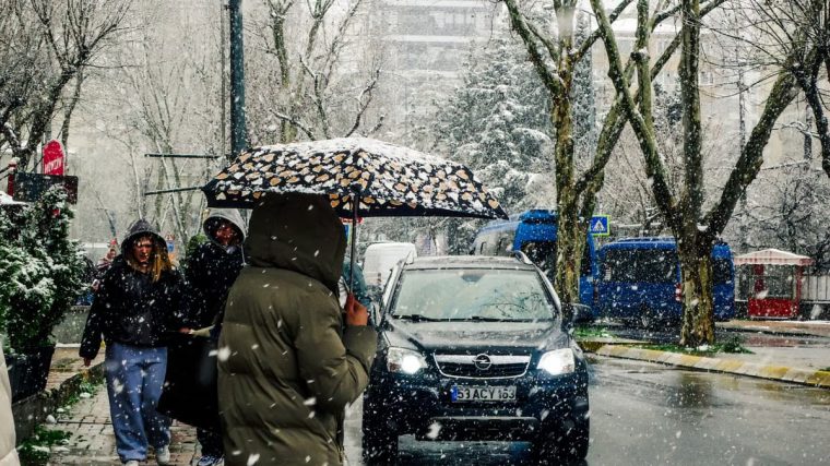 A snowy city street with people carrying umbrellas and cars passing by.